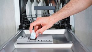 A man loads his dishwasher with one of the best dishwasher detergent brands.